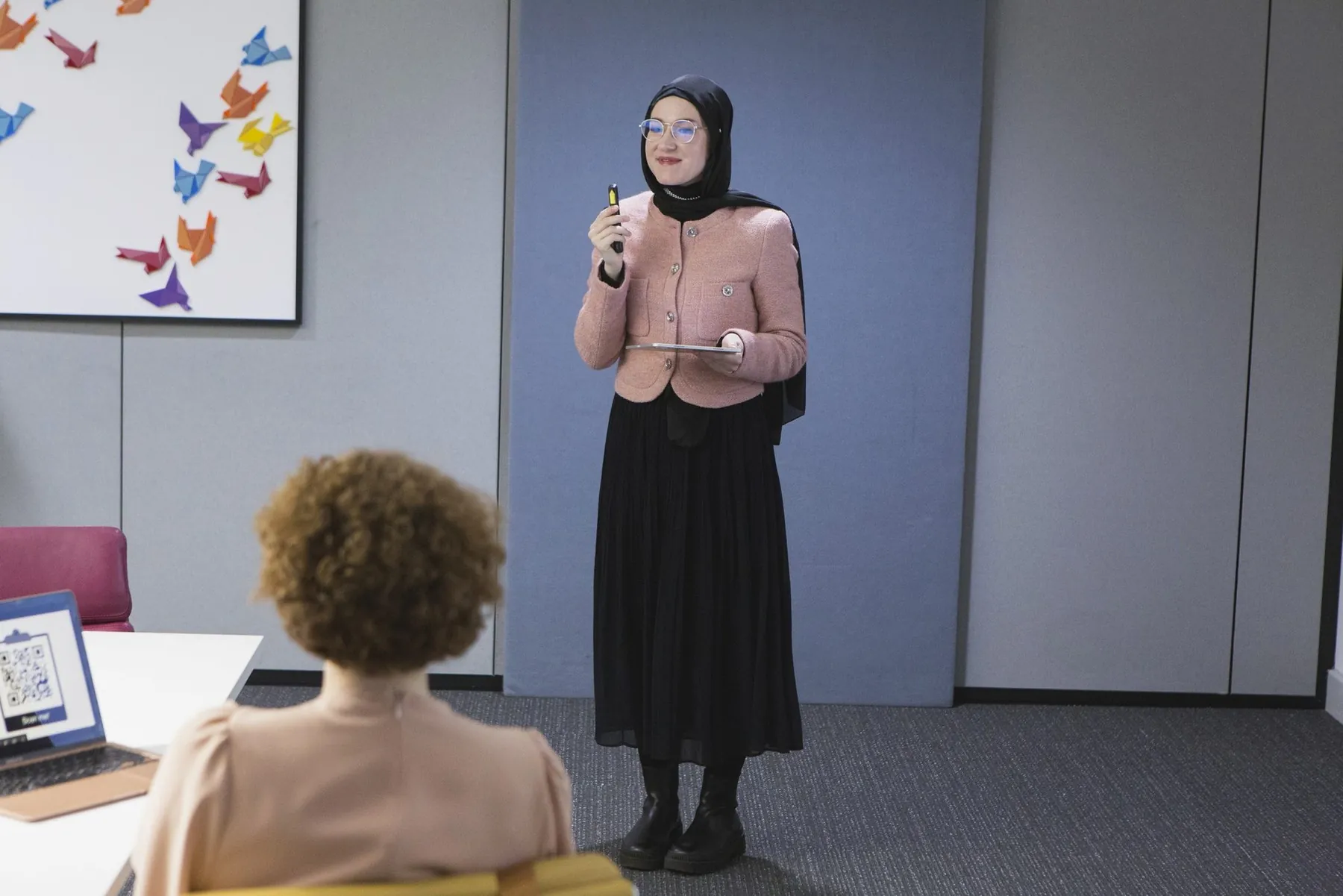 Agne presenting to a colleague in a meeting room, holding a clicker and a tablet.